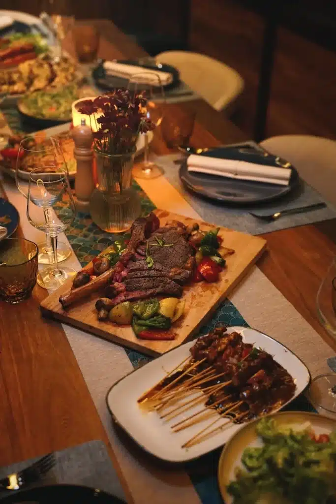 Candlelit onboard dinner spread with sliced steak, satay skewers, and grilled vegetables
