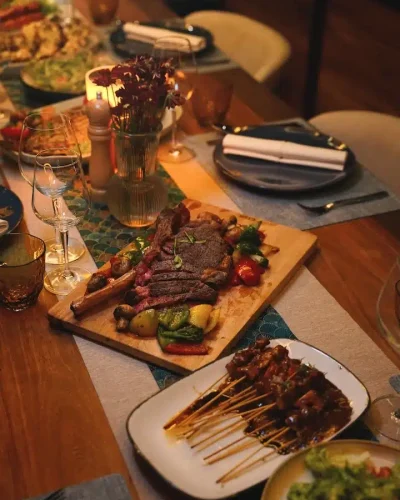 Candlelit onboard dinner spread with sliced steak, satay skewers, and grilled vegetables